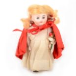 An early 20th Century French pocket full bisque miniature doll, in 'Little Red Riding Hood' outfit