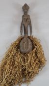 A tribal carved wood figure with sago palm leaf fringe, 66cm