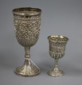 Two Indian embossed white metal pedestal cups, largest 19.5cm.