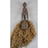 A tribal carved wood figure with sago palm leaf fringe, 66cm