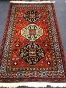 A Kazak style red ground rug, woven with three geometric medallions 204 x 127cm