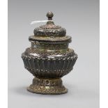 A Tibetan repousse white metal jar and cover, on detachable foot, 11.1cm.