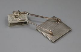 A pair of George V silver sugar nips, a silver match sleeve and a white metal compact.