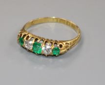 A George V 18ct gold emerald and diamond five stone half hoop ring, (stone chip), size P.