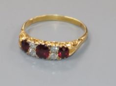 An early-mid 20th century yellow metal three stone ruby and four stone diamond ring, size S.