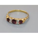 An early-mid 20th century yellow metal three stone ruby and four stone diamond ring, size S.