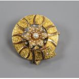 A yellow metal and seed pearl set circular 'belt and flower head' brooch, 25mm.