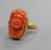 An antique yellow metal and oval coral ring, carved with the bust of a gentleman, size O.