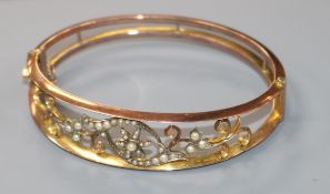 An Edwardian 9ct gold and seed pearl set open work hinged bangle.