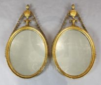 A pair of George III giltwood and gesso oval wall mirrors, with urn and bell husk crests, W.1ft 5in.