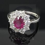 A white gold, ruby and diamond cluster ring, the oval cut central ruby bordered by ten round