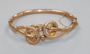 An early 20th century 9ct gold hinged bangle with scrolling motif.