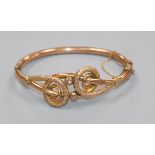 An early 20th century 9ct gold hinged bangle with scrolling motif.