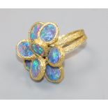 A 1970's? textured 18ct gold and eight stone oval black opal set dress ring, size K/L.