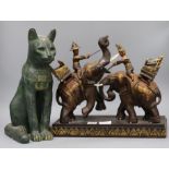 A Thai carved wood group of figures with fighting elephants, a bronzed eagle and a cat