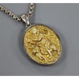 An Indian white and yellow metal oval locket embossed with a deity, on a white metal chain, locket