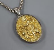 An Indian white and yellow metal oval locket embossed with a deity, on a white metal chain, locket