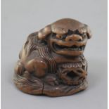 A Japanese wood netsuke of a shishi, seated on a rock, 19th century, its paw and chin resting upon a
