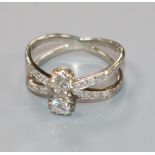 A white metal and two stone diamond set split shank ring, with diamond set shoulders, size K.