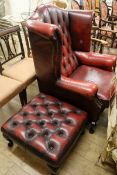 A buttoned red leather wing back armchair and footstool