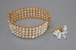 An Indian? yellow metal and baroque pearl set hinged bangle, with pearl set tassle safety chain.