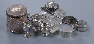 A silver tea strainer, three miniature silver trophy cups, a silver pill box, napkin ring, scent