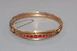 An early 20th century yellow metal and graduated red stone (including doublets) set hinged bangle.