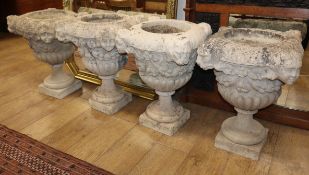 A set of four reconstituted stone urns, with masks, fruiting swags and demi fluted bases, raised