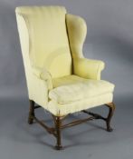 A George II mahogany wing armchair, with yellow fabric upholstery and cabriole legs, with turned H