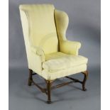 A George II mahogany wing armchair, with yellow fabric upholstery and cabriole legs, with turned H
