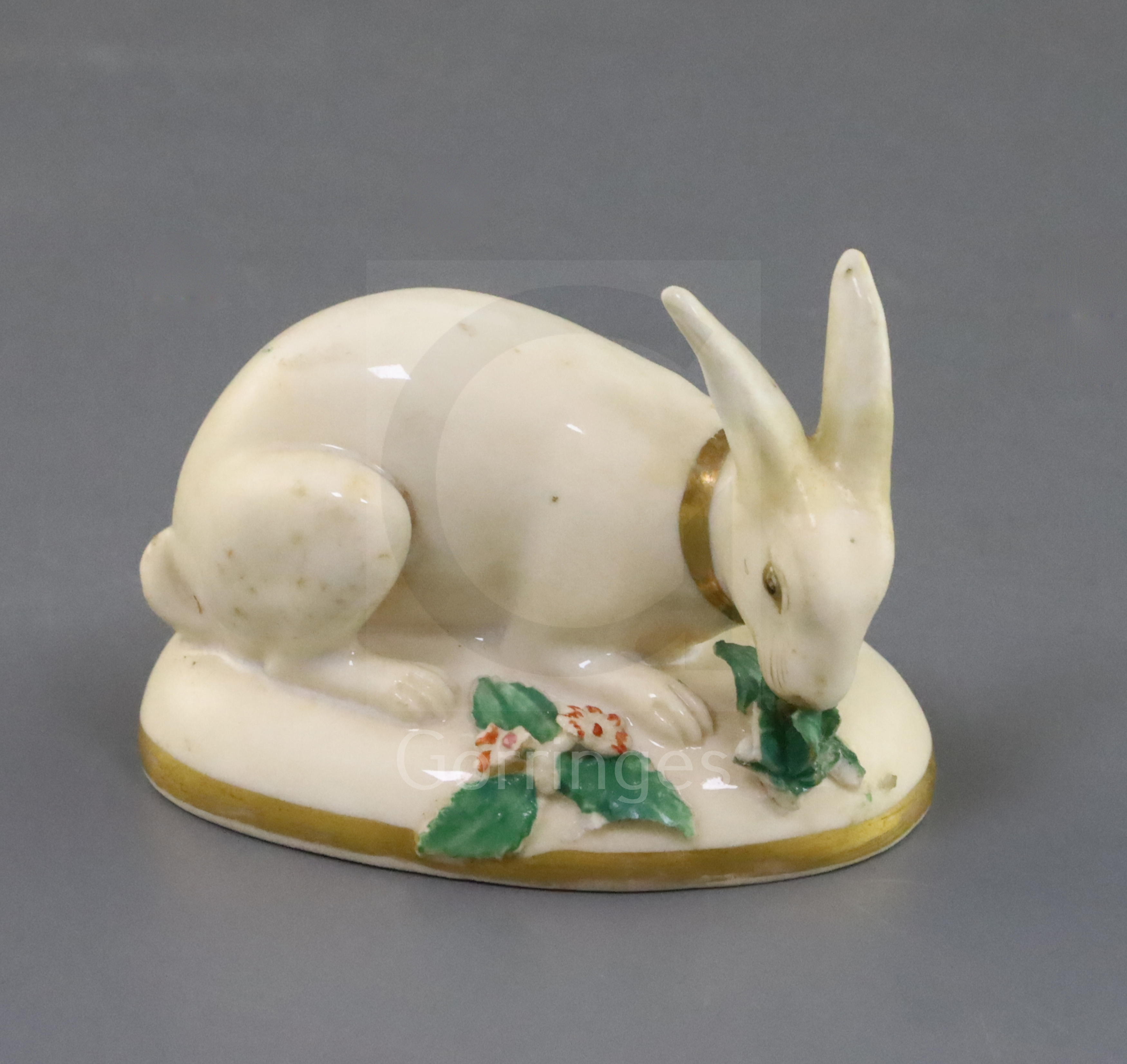 A Rockingham porcelain figure of a rabbit, c.1830, in cream and gilt eating green leaves, on an oval