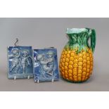 A Minton Majolica pineapple jug and two putti blue-glazed tiles tallest 12.5cm