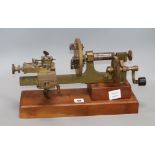 An early 20th century brass and steel clockmaker's lathe, on mahogany plinth