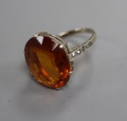 A white metal and oval cut citrine ring with diamond set shoulders, size K.