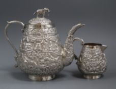 An Indian embossed white meta teapot and matching cream jug.