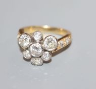 An 18ct and seven stone diamond cluster ring, with diamond set shoulders, size K/L.