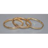 An engraved 14k yellow metal hinged bangle and two other hinged bangles.