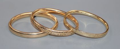 An engraved 14k yellow metal hinged bangle and two other hinged bangles.