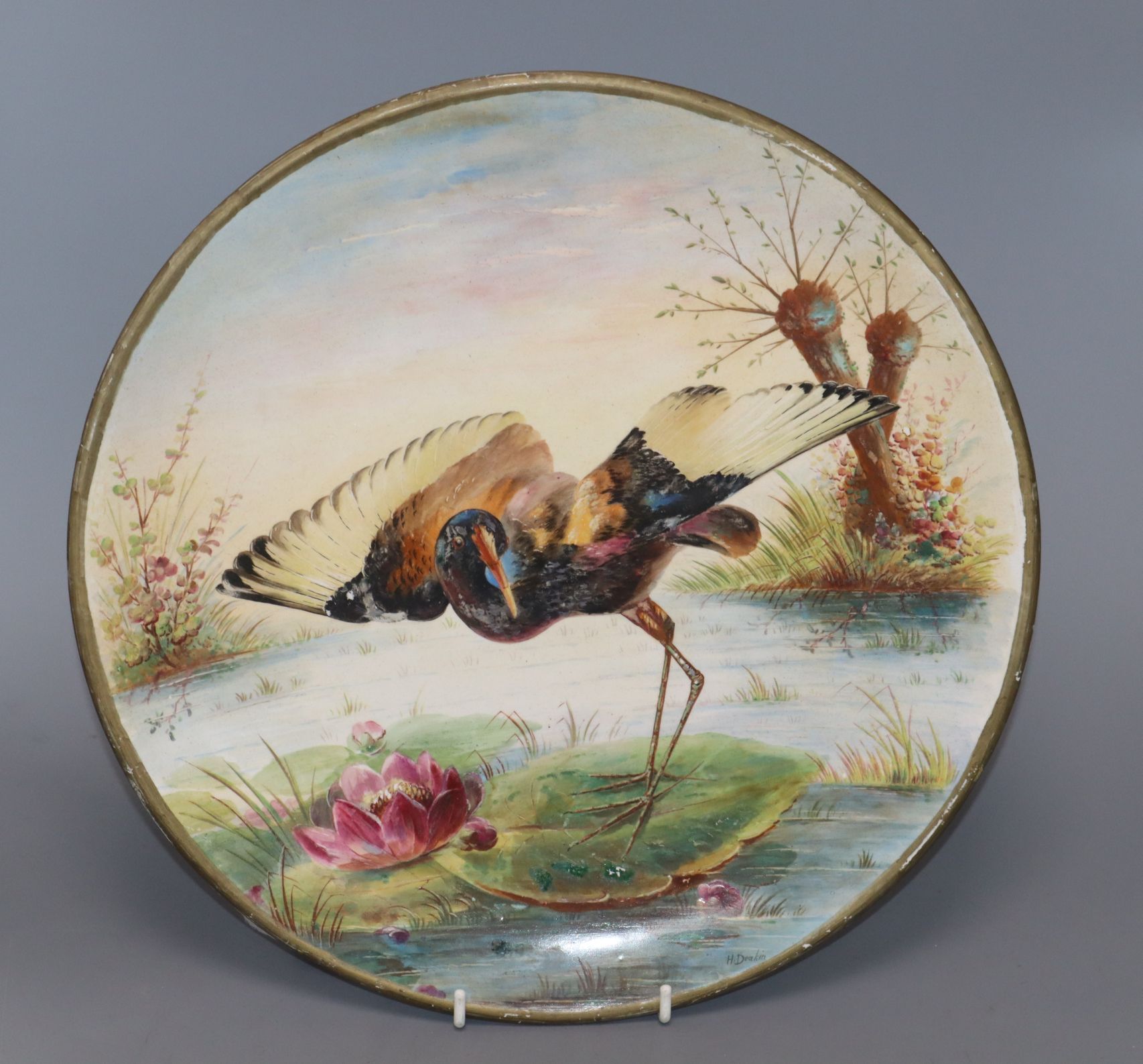 A ceramic charger painted with a Jacana standing on a lily pad by H. Deakin, Dia 32cm (worn)