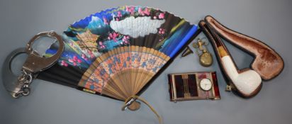 A minaudiere with timepiece, a meerschaum pipe in case, pair of handcuffs and key, a Chinese fan,