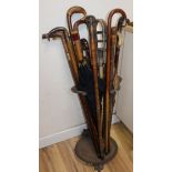 A collection of walking sticks, canes, shooting sticks, parasols and a cast iron stick stand