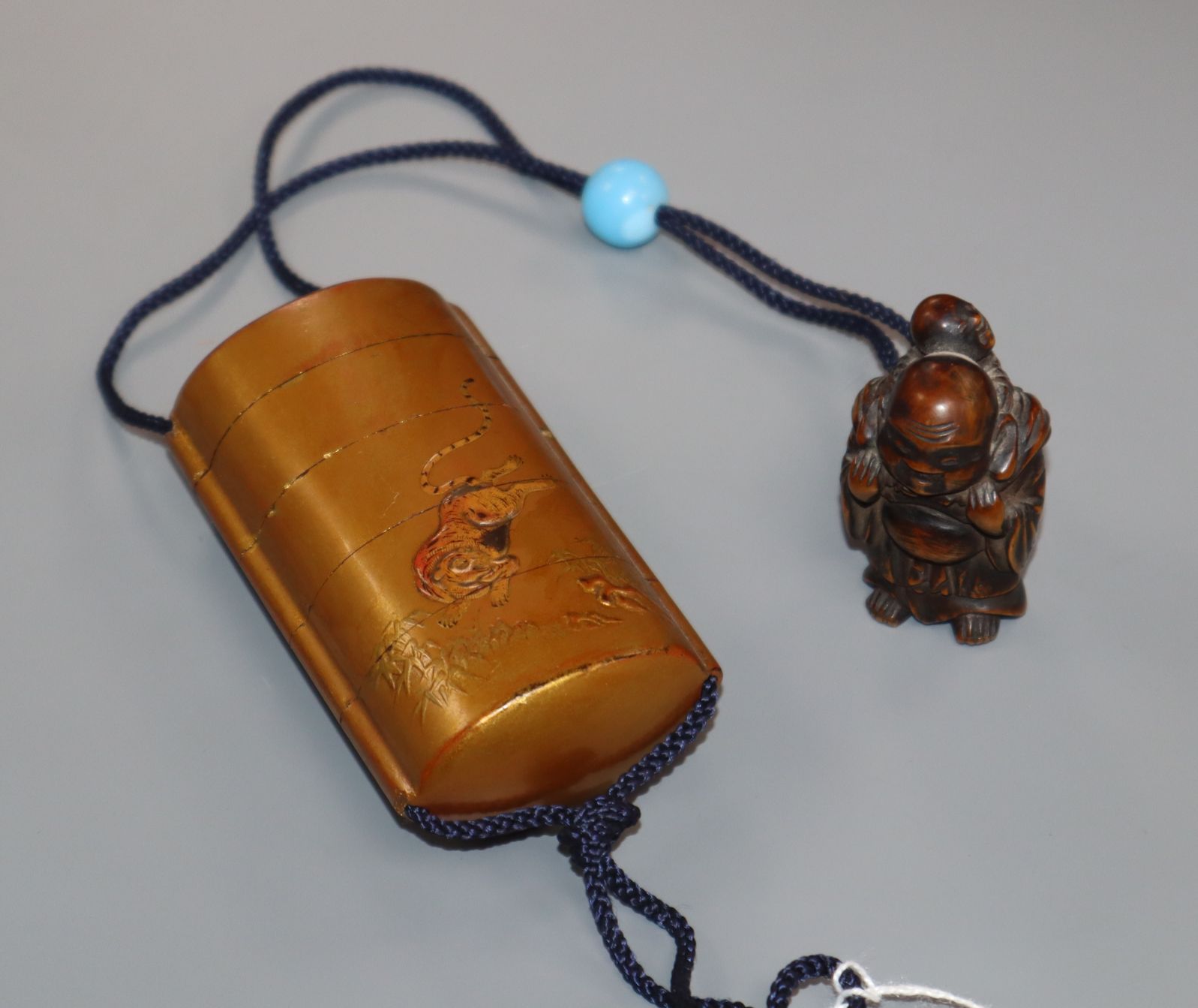 A Japanese gold lacquer four case inro with relief tiger and a hotei carved wood netsuke and blue