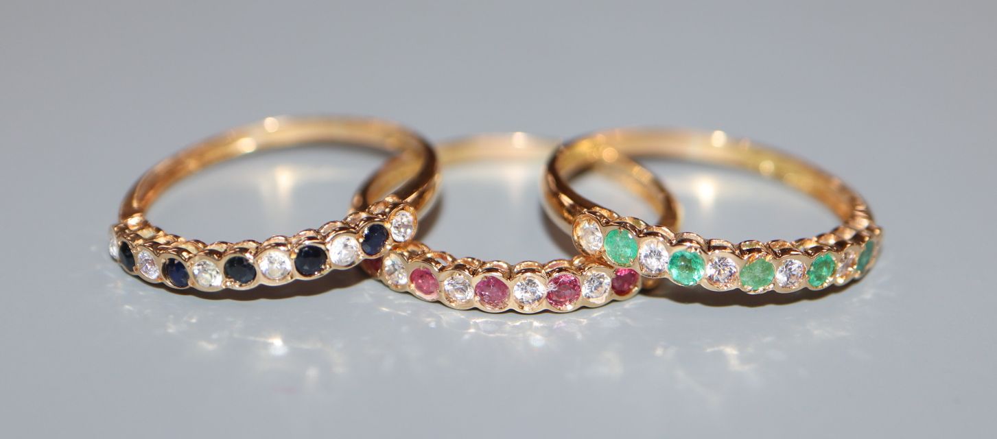 A modern suite of three yellow metal and gem set rings, including emerald, ruby and sapphire, size