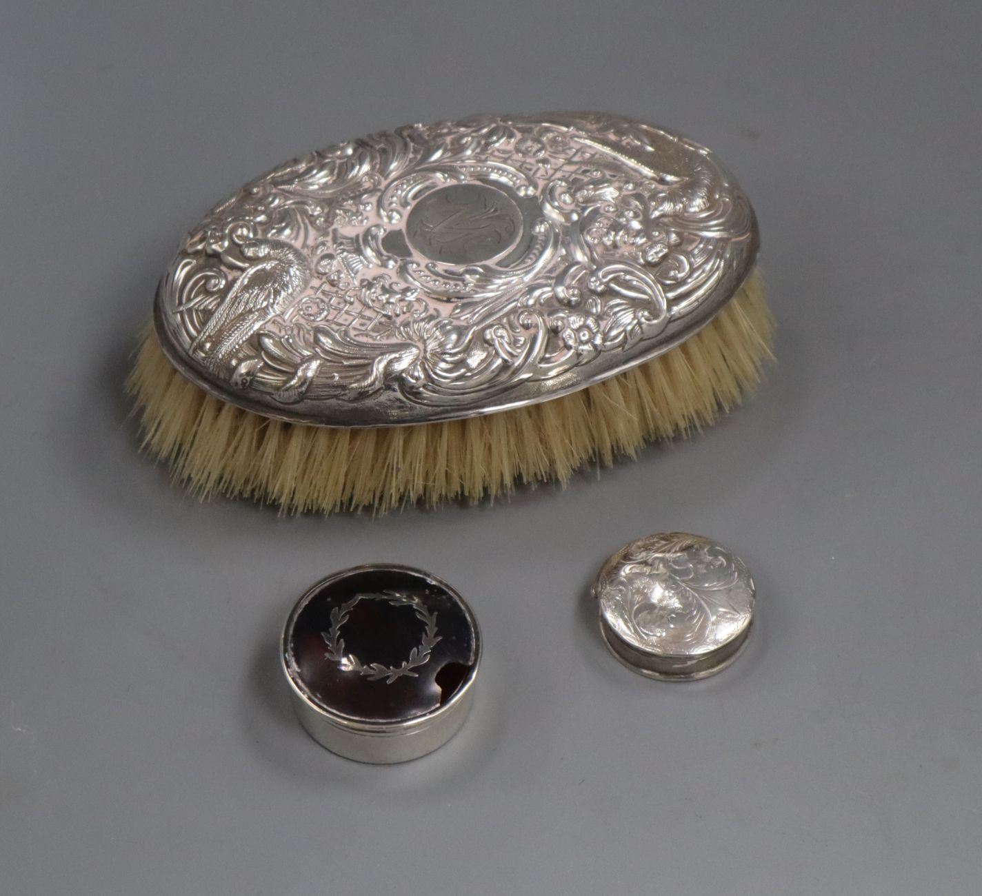 An embossed white metal clothes brush and two silver pill boxes (one a.f.).