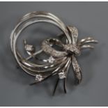 A modern 585 white metal and diamond set scroll bow brooch, 35mm.