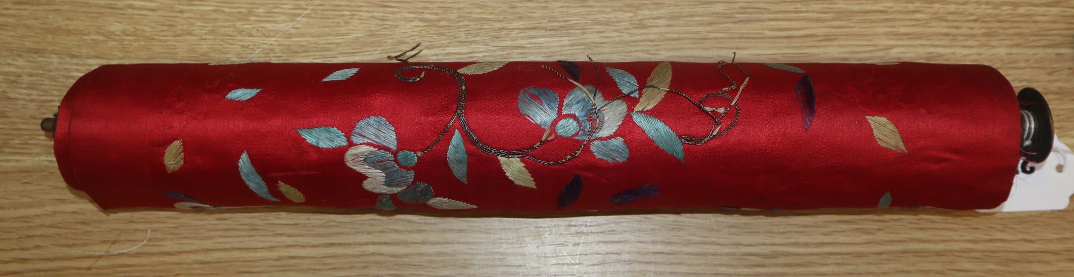 A Chinese red silk banner embroidered with figures, flowers, insects and calligraphy, on brass-