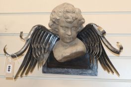 A reconstituted stone head of a putti with ironwork feathers, wall mounted W.45cm