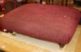 A large rectangular red upholstered stool on brass castors W.90cm