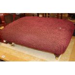 A large rectangular red upholstered stool on brass castors W.90cm