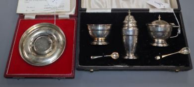 A three-piece silver condiment set and a silver Churchill commemorative dish (both cased)
